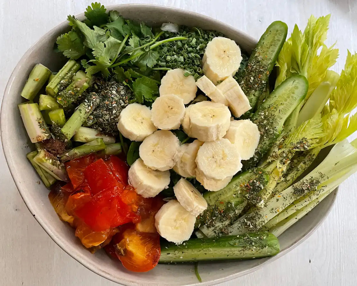 Bananenscheiben auf Blattgrün mit Gurke, Sellerie und Tomaten in Schüssel