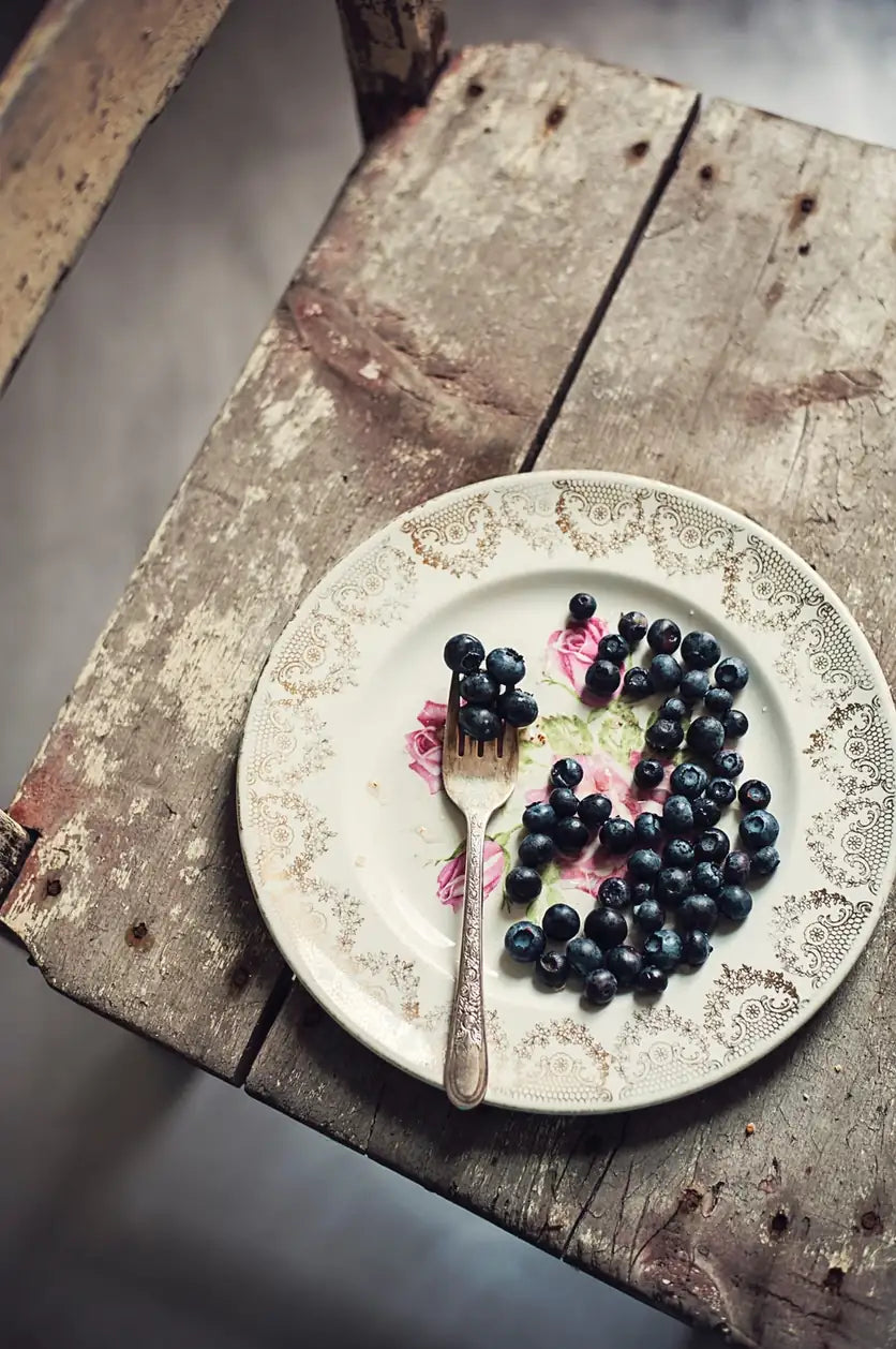 Blaubeeren mit Gabel auf verziertem Porzellanteller auf Holzhocker