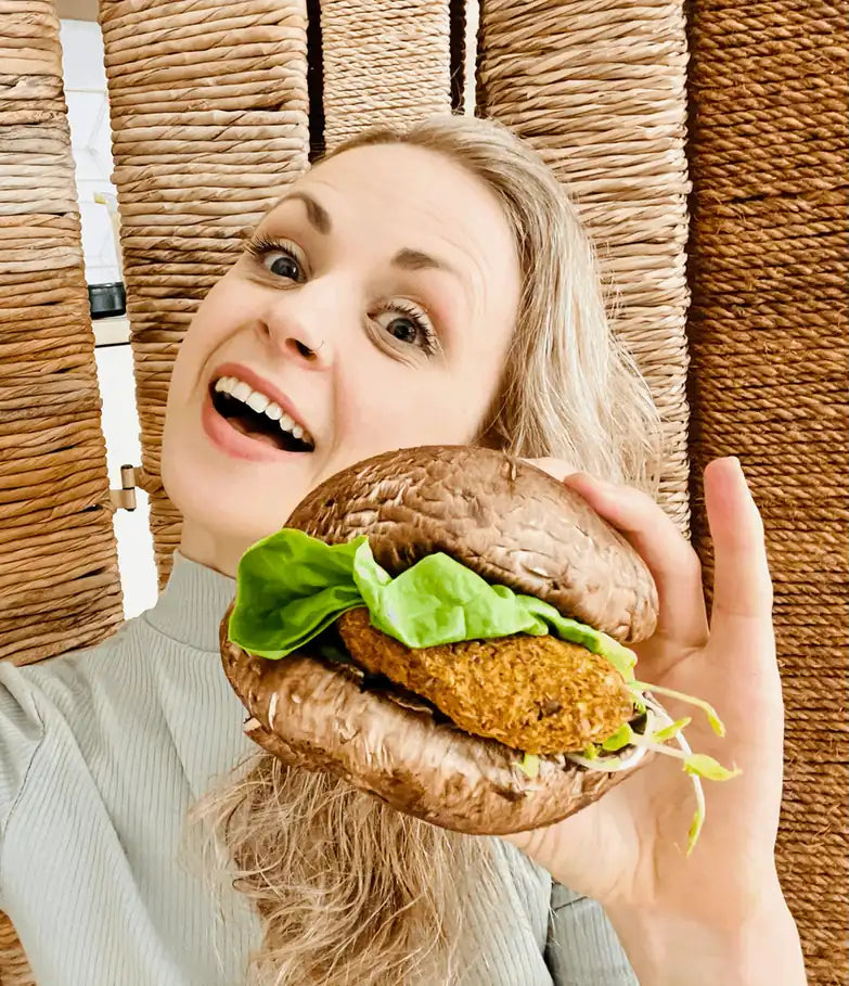 Lachende Frau hält rohveganen Burger mit Portobello-Bun in der Hand