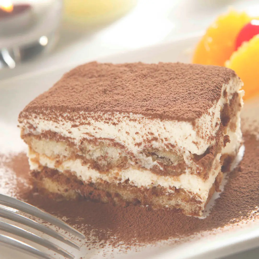 Stück Tiramisu mit Kakaopulver auf Teller neben Gabel