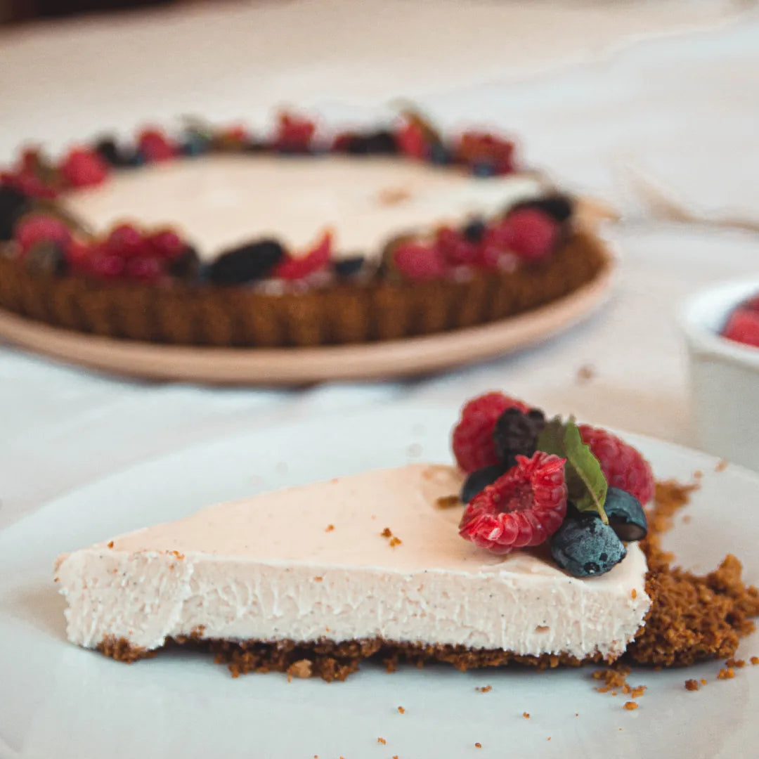 Stück Beerentarte mit Himbeeren und Blaubeeren vor ganzer Tarte