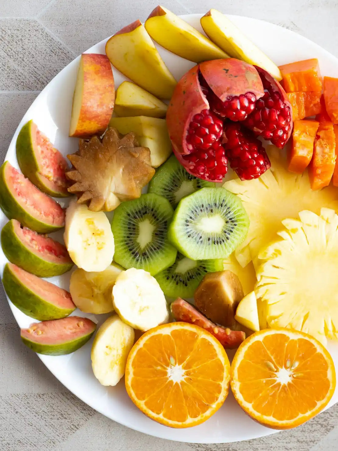 Großer Obstteller mit Orangen, Kiwi, Ananas, Granatapfel und Apfelspalten