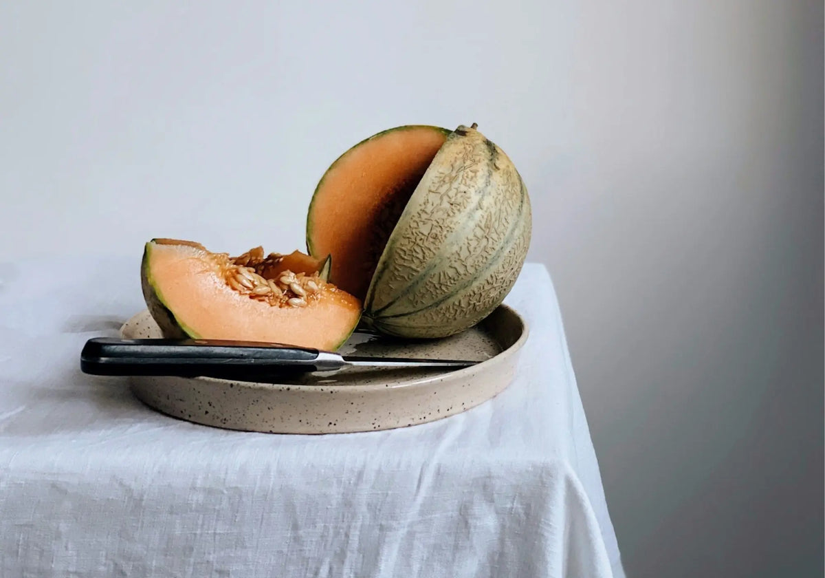 Aufgeschnittene Cantaloupe-Melone mit Messer auf Teller und weißem Tuch