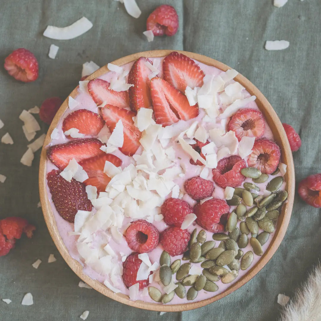 Rosa Himbeerjoghurt in Holzschale mit Erdbeeren, Kokoschips und Kürbiskernen