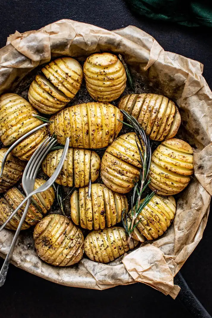 Fächerkartoffeln mit Kräutern auf Backpapier in schwarzer Pfanne