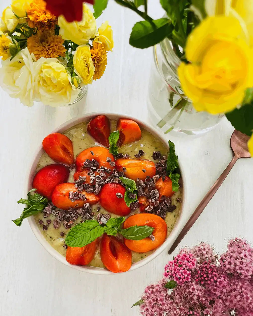 Smoothie Bowl mit Steinobst, Erdbeeren, Kakaonibs und Minze neben Blumen