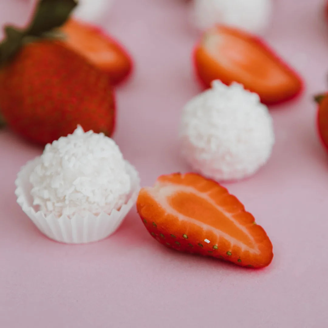 Kokospralinen in Papierförmchen neben Erdbeeren auf rosa Untergrund