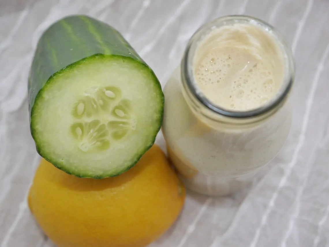 Halbierte Gurke, Zitrone und Glasflasche mit cremigem Tahini-Dressing