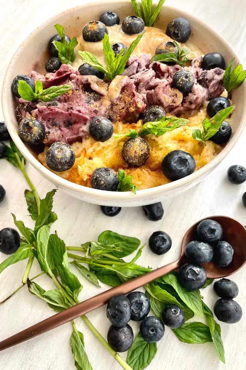 Bowl mit Blaubeeren, Beerencreme und frischer Minze, daneben ein Holzlöffel