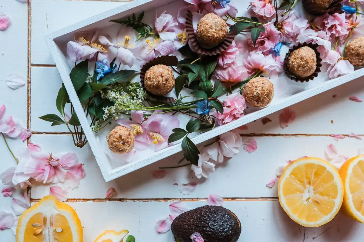Carrot Balls in weißer Holzkiste mit Blüten, daneben Zitrone und Avocado