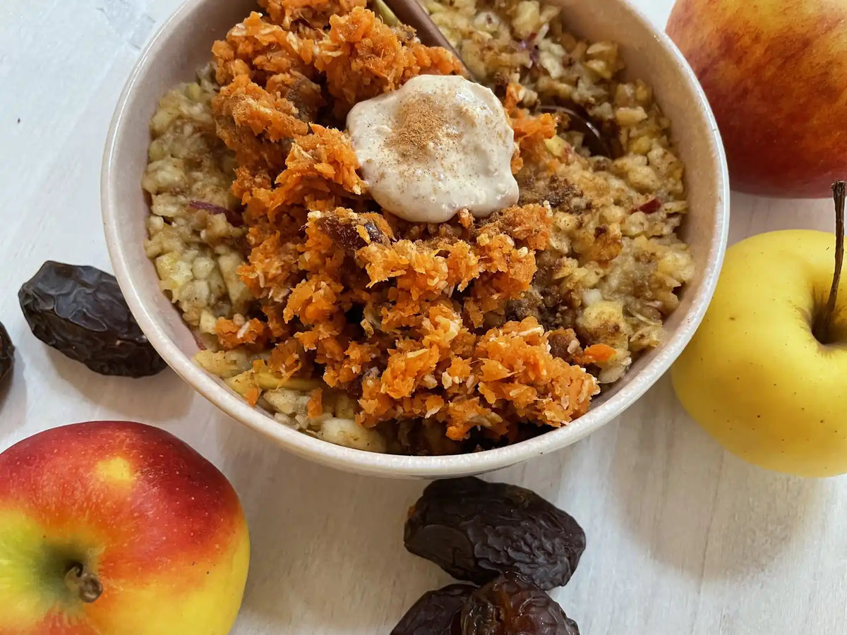 Rohes Porridge mit Karotten-Topping und Cashewmus, daneben Äpfel und Datteln