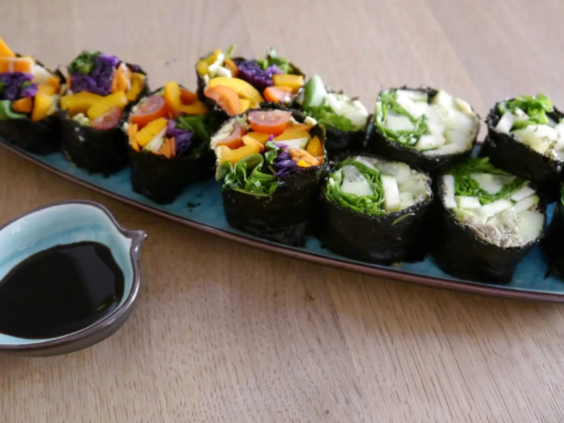 Gemüse-Sushi-Röllchen auf blauer Platte, daneben eine dunkle Dipsauce