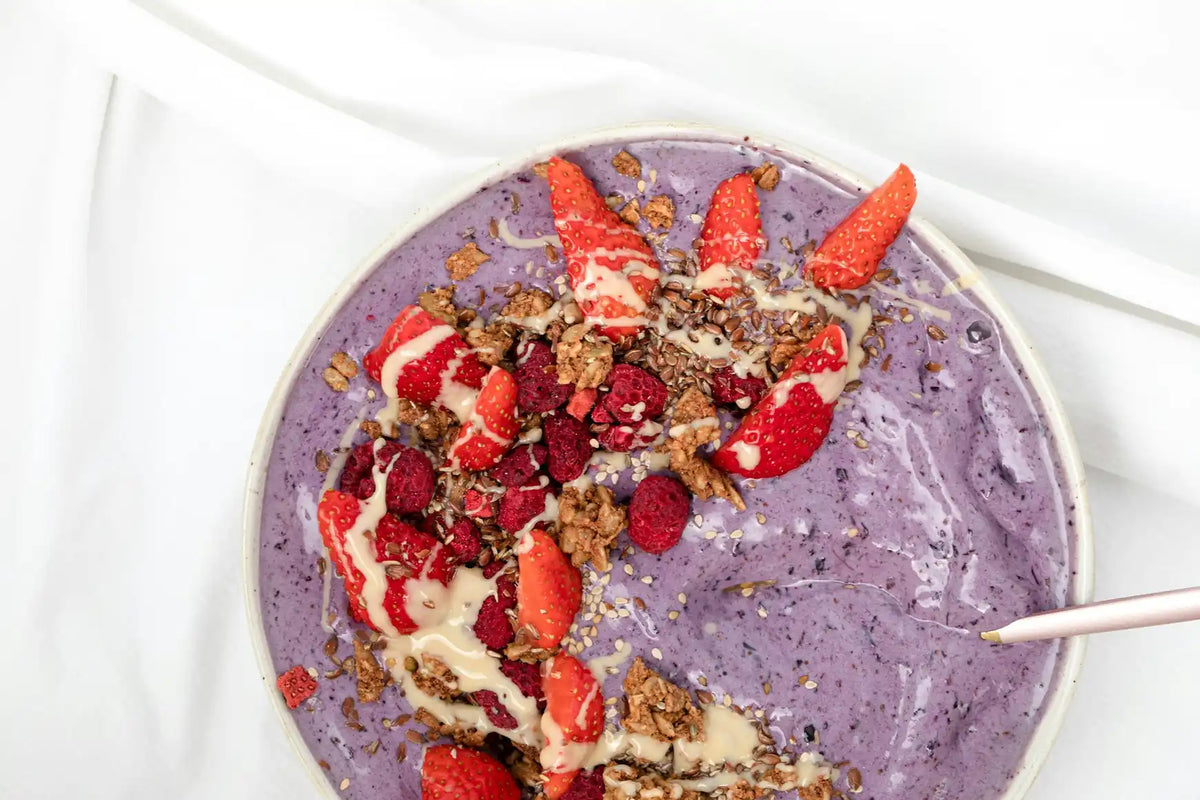 Lila Smoothie Bowl mit Erdbeeren, Himbeeren und Granola auf weißem Tuch