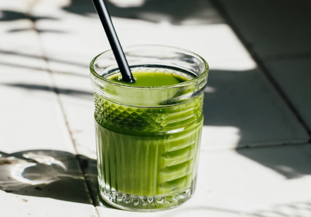 Grüner Saft in einem Glas mit schwarzem Strohhalm im Sonnenlicht