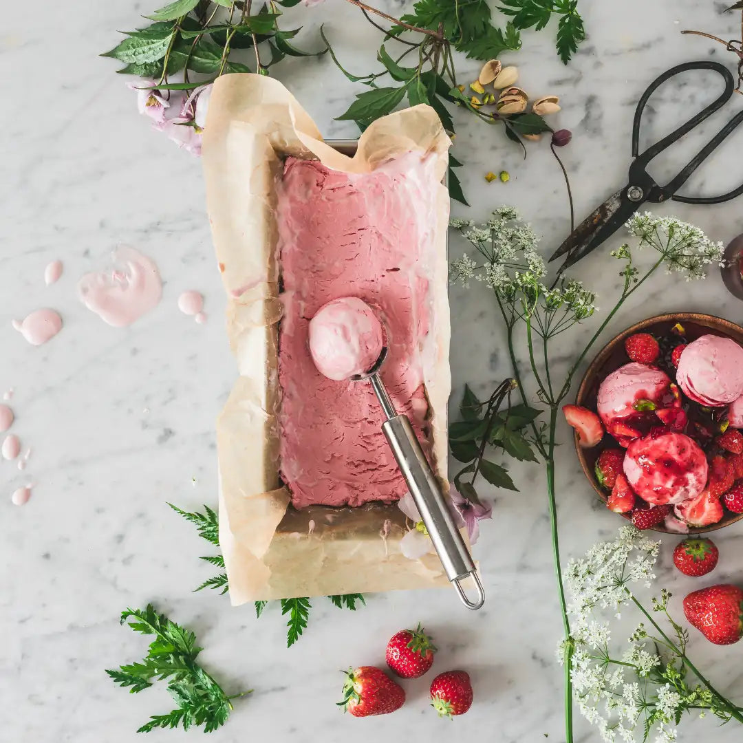 Rosa Beereneis in Kastenform mit Eisportionierer und frischen Erdbeeren