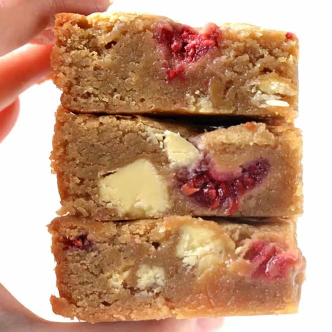 Drei gestapelte White Choc Raspberry Blondies mit Himbeeren, in der Hand gehalten