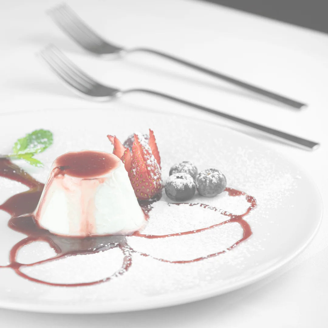 Gestürzte Panna Cotta mit Beerensauce, Erdbeere und Heidelbeeren auf weißem Teller