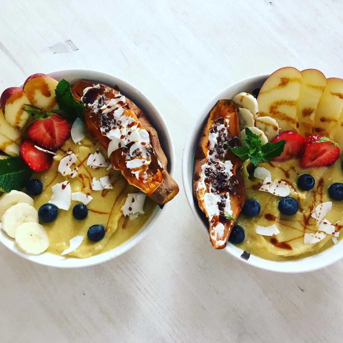 Zwei gelbe Smoothie Bowls mit Papaya, Banane, Erdbeeren und Heidelbeeren