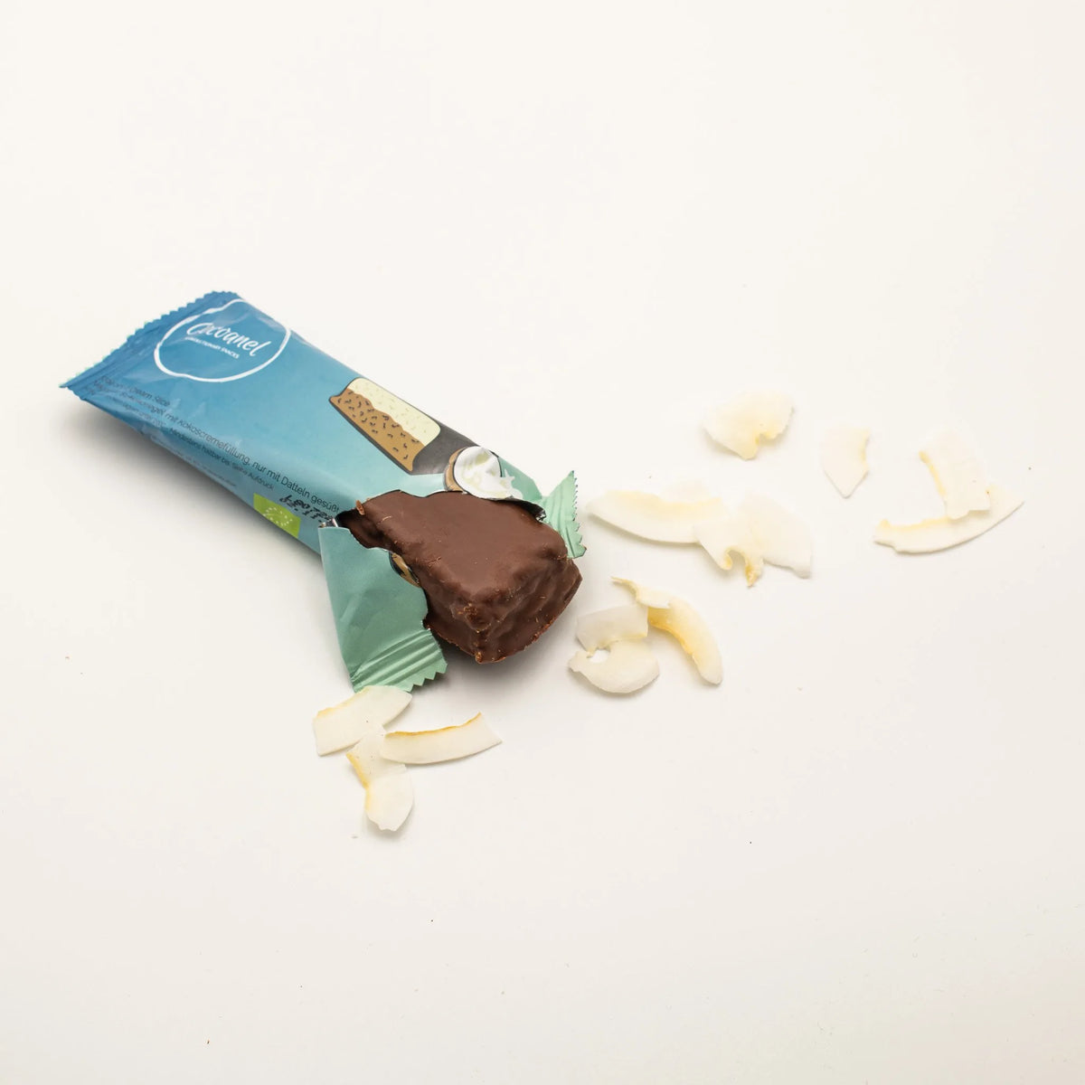 Cocoanel Riegel in blauer Verpackung, angebrochen, daneben Kokoschips