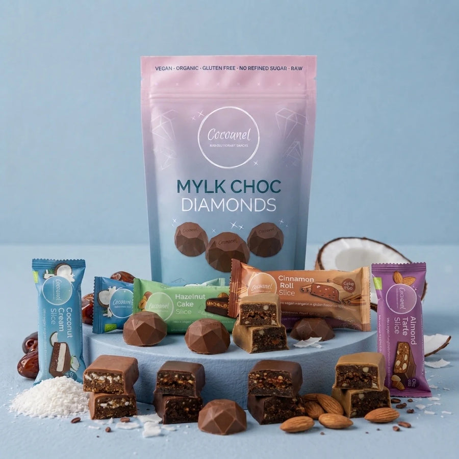 Discovery Box mit Mylk Choc Diamonds und vier Slices-Sorten auf hellblauem Podest, daneben Mandeln und Kokosnuss