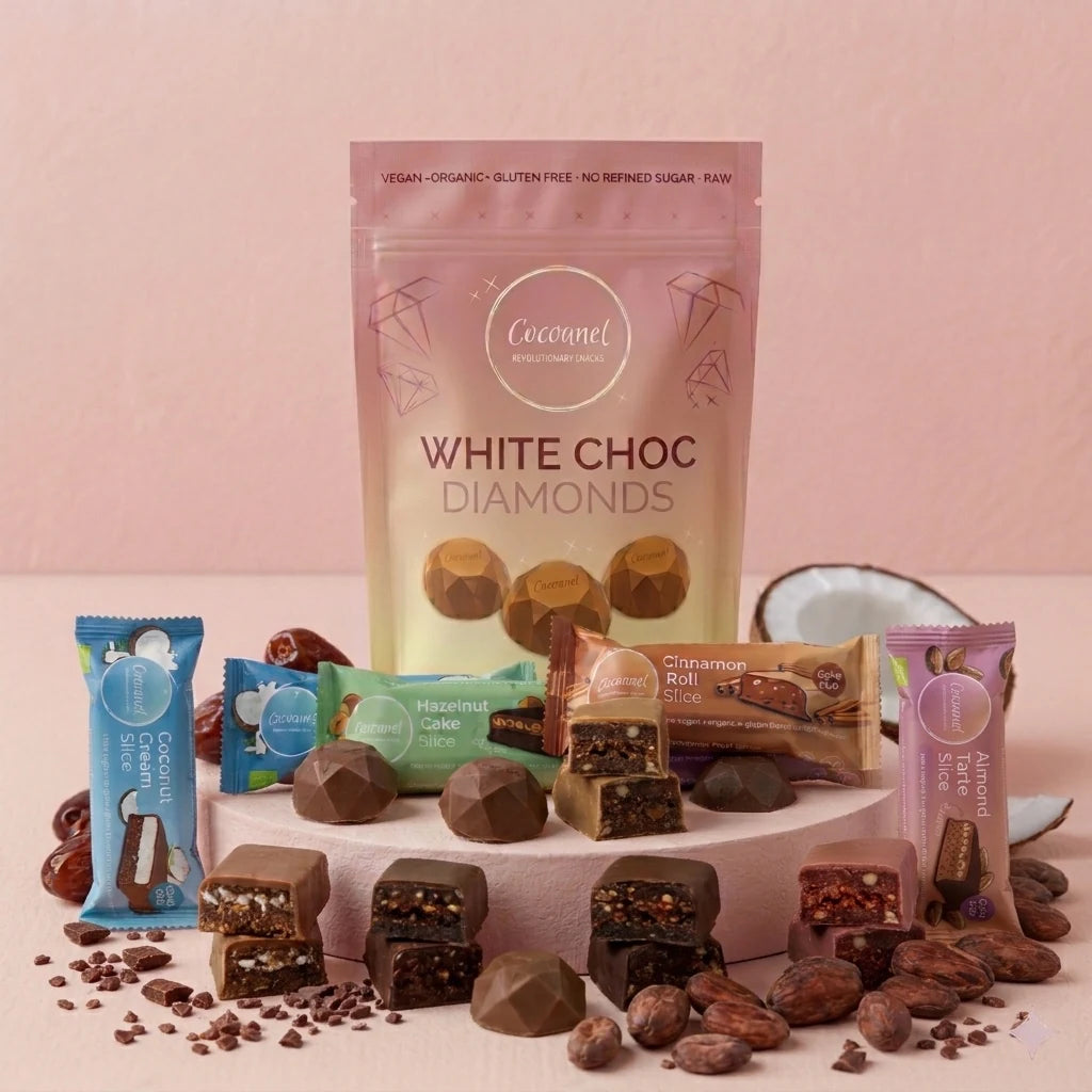 Discovery Box mit White Choc Diamonds und vier Slices-Sorten auf hellem Podest, daneben Kakaobohnen und Kokosnuss