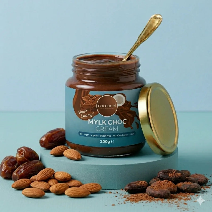 Mylk Choc Cream: geöffnetes Glas mit Löffel, dazu Datteln, Mandeln und Kakaobohnen